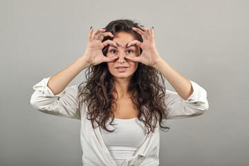 Making glasses of fingers, looking at camera and smiling, funny, hold hands near eyes, imitating binoculars, holding arm eyebrows, through imaginary binocular, grimacing, mask with hand. Young woman