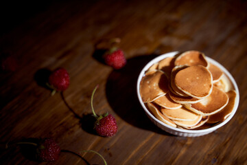 mini pancakes with strawberries in a white plate on a dark brown wooden table. With copy space