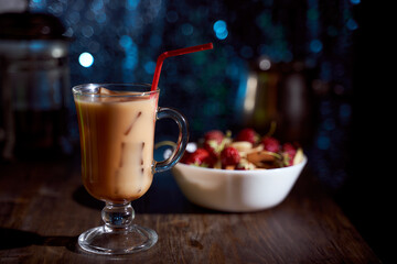 Ice coffee in a latte glass with cream poured over, ice cubes and beans on dark wooden table. black background with copy space.