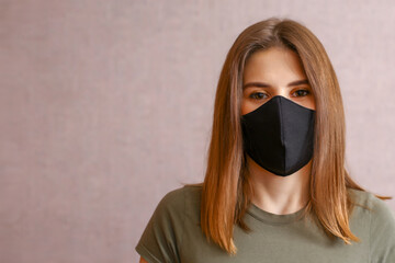 brunette in a black mask. a young woman in a cloth mask on a light background. protection against coronavirus infection, covid-19.