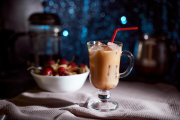 Ice coffee in a latte glass with cream poured over, ice cubes and beans on a gray towel. black background with copy space.