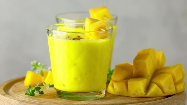 Yellow Indian mango yogurt drink Mango Lassi or smoothie with turmeric and saffron. Healthy probiotic Indian cold summer drink moving slowly on light gray background