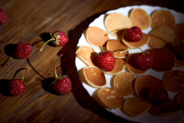 mini pancakes with strawberries in a white plate on a dark brown wooden table. close up. With copy space