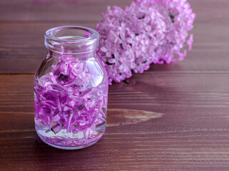 Obraz na płótnie Canvas A bottle with aromatic tincture and lilac flowers for Spa and aromatherapy on a wooden background. Copy space