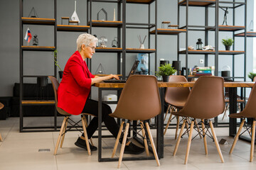 beautiful stylish aged woman in a red jacket works in the office with a laptop