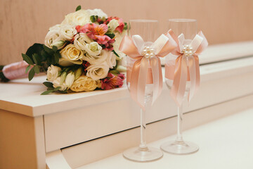 a wedding bouquet lies next to glasses decorated with pink ribbons.