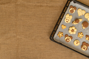 homemade cookies in the shape of dog, heart, elephant, butterfly, snowflake, slug, turtle, heart, rabbit, chamomile and owl in the tray. burlap cloth with copy space and lettering part. animal shaped