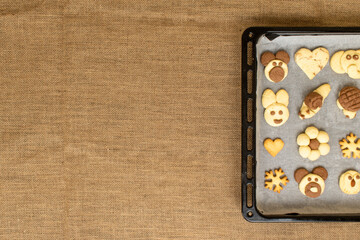 homemade cookies in the shape of dog, heart, elephant, butterfly, snowflake, slug, turtle, heart, rabbit, chamomile and owl in the tray. burlap cloth with copy space and lettering part. animal shaped