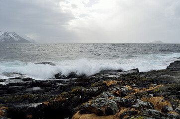 stormy windy day by the sea shore with majestic mountain in the distance on the island of Senja