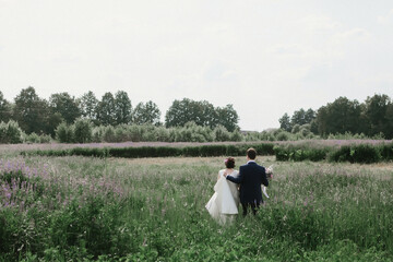 a young couple holding hands and holding a wedding bouquet in their hands goes across the green field into the distance