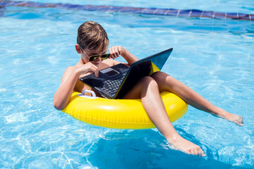 Kid boy using laptop in the swimming pool. Technology, summer and vacation concept