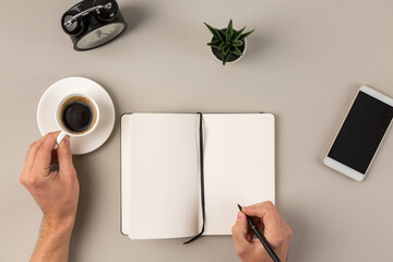 Obraz premium Overhead view of man hands writing in blank notepad and holding cup of coffee on abstract gray office desk