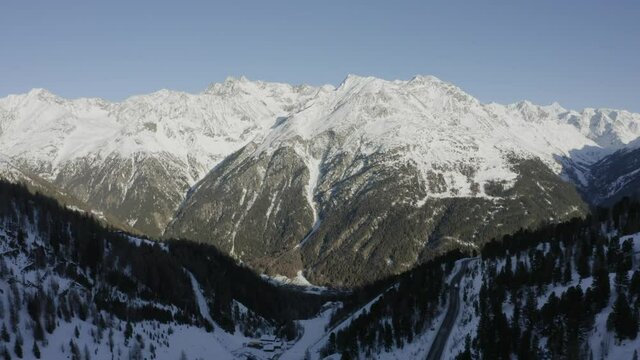 Flying through valley in Austrian Alps with view of sunlight falling on several snow covered mountains
