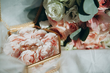 golden shiny wedding rings lie in a decorative box next to a wedding bouquet