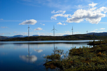 Fototapeta na wymiar windmill farm on mountain top reflecting in the lake water on sunny blue autumn day