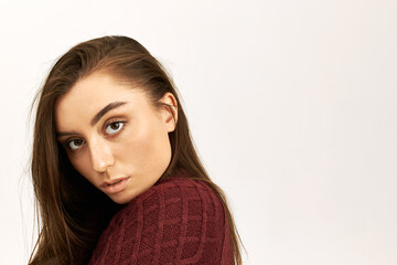 Close up profile image of attractive young dark haired woman wearing knitted jumper posing isolated against blank copy space background, looking at camera with serious confident facial expression