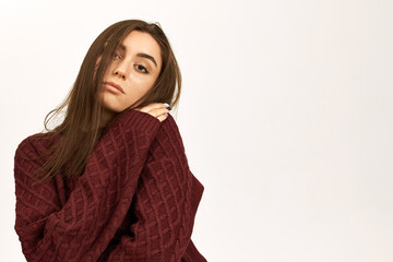 Winter, season, clothing and knitwear concept. Isolated shot of stylish cute young woman freezing from cold because heating turned off, trying to warm up in knitted sweater, hugging herself