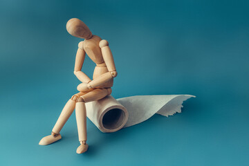 Wooden figure sit on a roll of toilet paper. Concept of the problem with digestion.