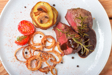 fresh grilled bbq beef meat rib eye steak on white plate with baked potatoes, mushrooms, tomatoes,fried onion, hot chili pepper and rosemary