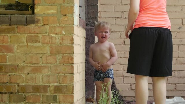 Little boy crying with mother hysterics naked toddler boy 2 years old with broom play in backyard slow motion