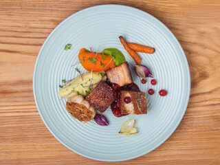pork belly with cranberry sauce, baked garlic and dumplings of mashed potatoes, carrots and peas decorated with microgreens