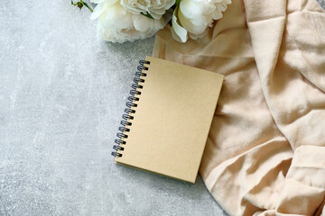 Kraft paper notebook or wedding photo album with peonies on concrete stone table. Flat lay, top view.