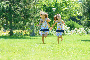 Naklejka na ściany i meble Two little sister run on a green lawn in a park