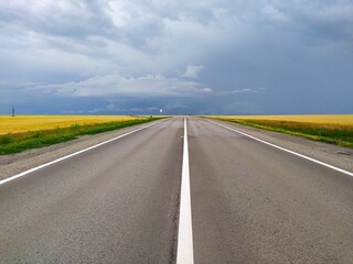 paved road with white markings going into the distance and past fields