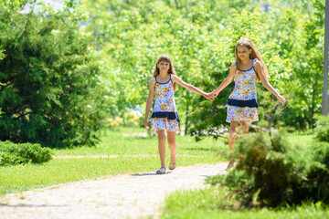 Naklejka na ściany i meble Two sisters together walk in a beautiful city park