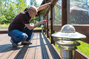 Male painter with a paint brush in his hands. A man, Caucasian, paints a wooden terrace. Painting works