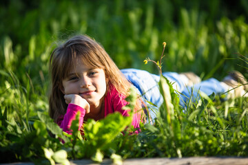 Cute pleasant little girl is lying in the green grass.