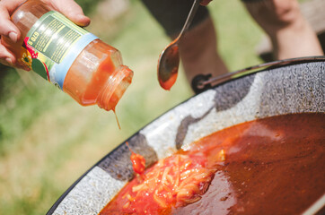 Adding ingedients into goulash soup on the garden party.