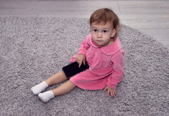 Fototapeta premium beautiful little girl with a smartphone on the carpet in her room.
