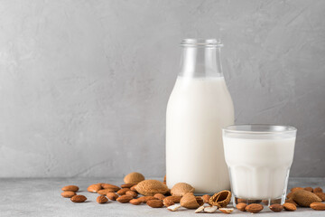 Almond milk in a bottle with glass and almond nuts on concrete background. Vegan dairy free plant milk