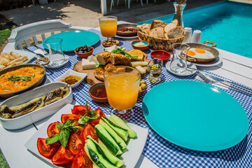 Concept promotional morning breakfast in the hotel, tasty Egg Benedict,Turkish and French Breakfast, tea and orange juice. near swimming pool in the garden