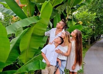 Cheerful, happy family, father, mother, son and daughter enjoying walk in banana palm leaves....