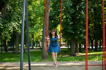 adorable teenager girl portrait in swing children playground space in summer time park outdoor space smiling and happiness emotion