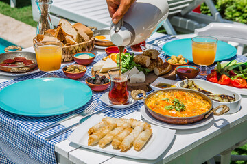 Fototapeta na wymiar Concept promotional morning breakfast in the hotel, tasty Egg Benedict,Turkish and French Breakfast, tea and orange juice. near swimming pool in the garden
