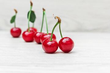 Blurred row of red berries of tasty juicy cherry with green leaves on a white wooden close-up. Photo on a wooden background with free space.