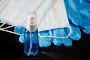 Tube with blue sanitizer, blue medical masks and blue medical gloves on a black background