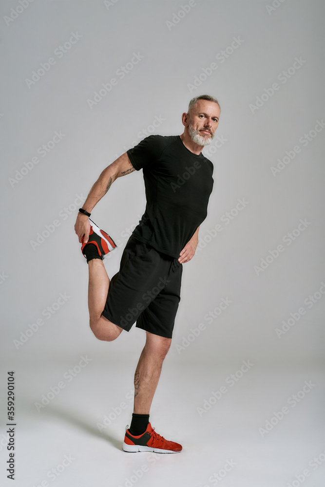 Wall mural full length shot of middle aged muscular man in black sportswear looking at camera while stretching 