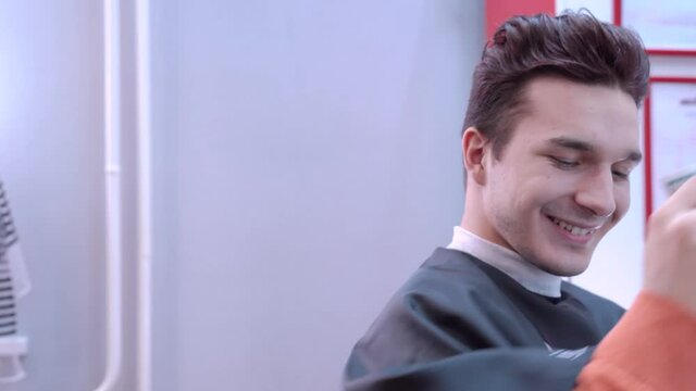 Young man with stylish hairstyle, sinister expression and sly smile sticks his hand out from under black robe and gives money as a bribe or as payment for services to woman with pearl bracelet.