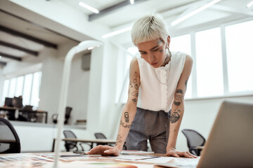 Creative occupation. Young stylish tattooed female designer working on new project while standing...