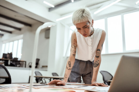 Creative occupation. Young stylish tattooed female designer working on new project while standing near office desk