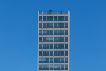 Outdoor sunny exterior elevation side view of Modern office tower with simply grid frame windows facade against background of blue sky.   