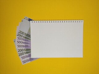Notepad with a copy space, 200,500 Euro bills peek out from under it.