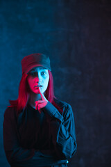 Pensive girl in cap with colorful neon lighting on dark background. Problem of choice concept with copy space.