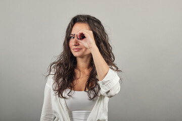 Fototapeta premium Making glasses of fingers, looking at camera and smiling, funny, hold hands near eyes, imitating binoculars, holding arm eyebrows, through imaginary binocular, grimacing, mask with hand. Woman