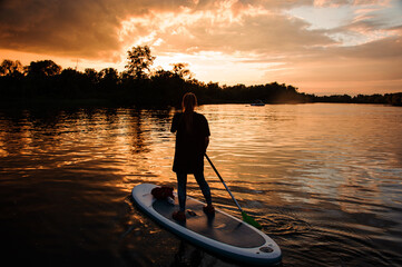 rear view of girl on sup board who floating on the river at sunset