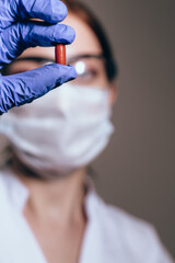 Blurred female scientist with protective mask holding capsule in first plan